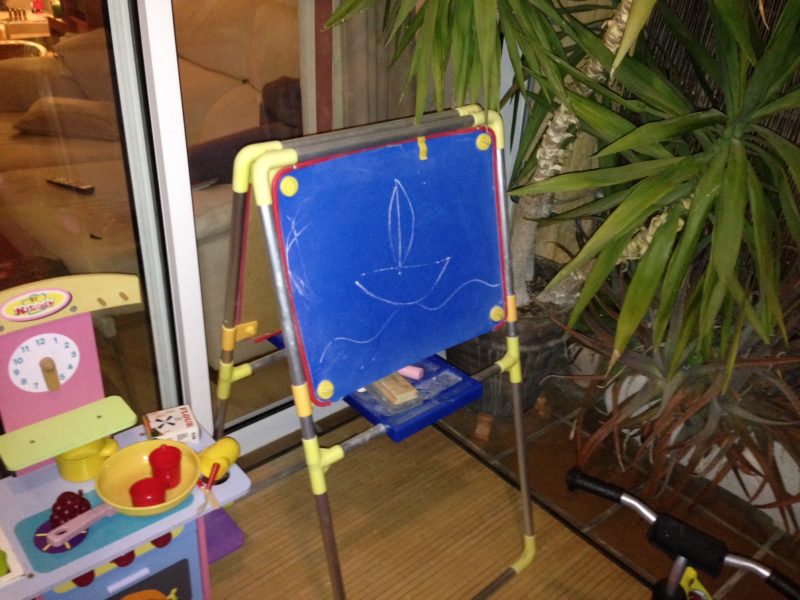 Ein mit Kreide gemaltes Segelboot auf einer kleinen blauen Tafel für Kinder