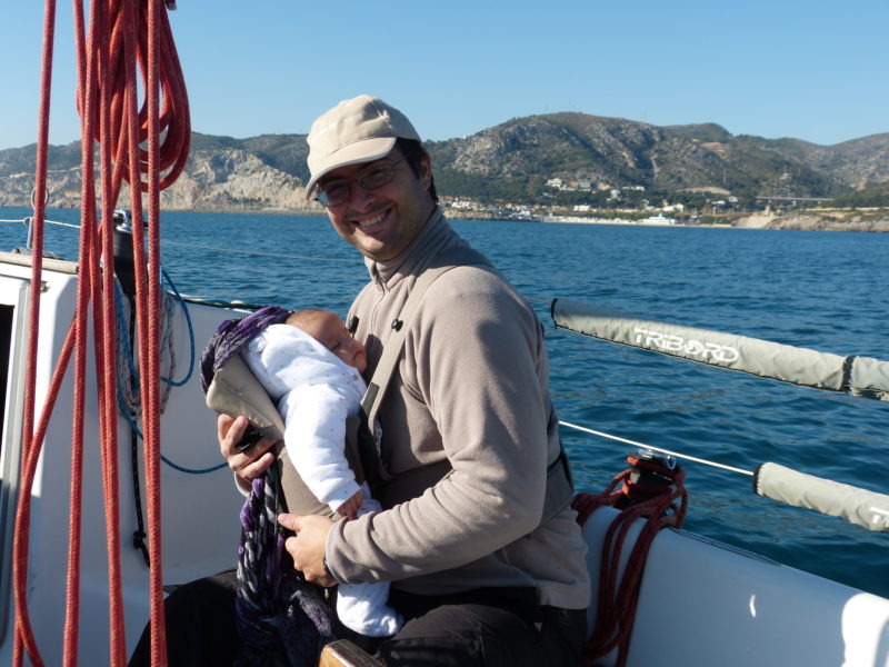 Vater an Bord eines Segelbootes mit einem Baby auf dem Arm