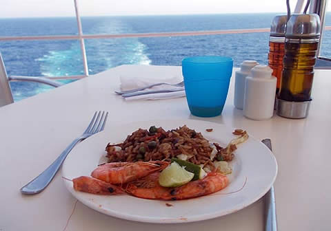 Ein Teller mit Lachs und Reis auf einem Tisch vor blauem Wasser