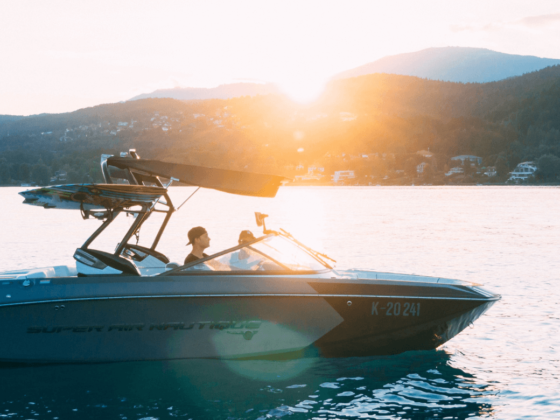 Personen auf einem Motorboot, welche bei Sonnenuntergang an einer bergigen Küste fahren
