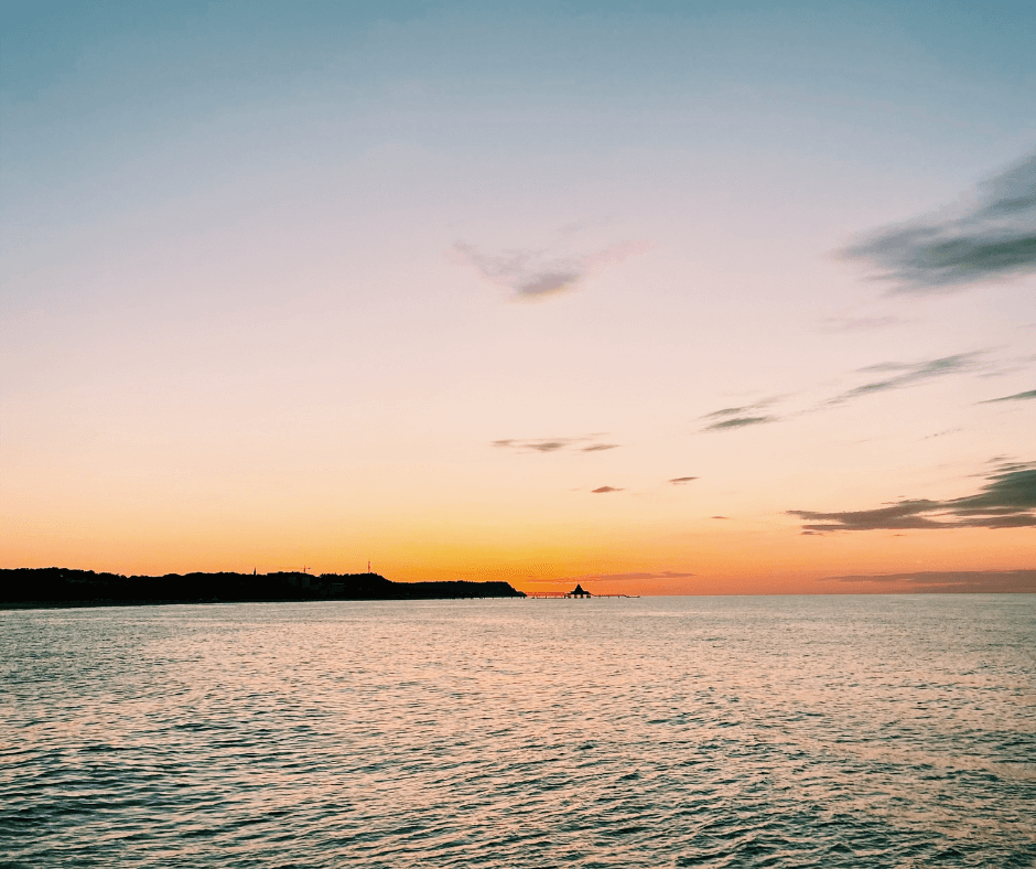 Das Meer bei Sonnenuntergang mit einem Teil der im Schatten liegenden Küste und einem Steg im Wasser 