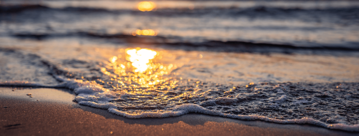 Sonnenuntergang der sich in der Wasseroberfläche des Meeres am Strand spiegelt