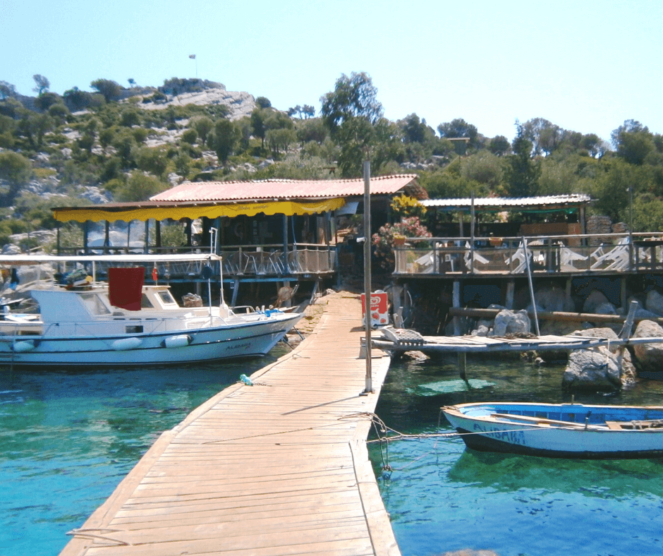 Segeltörn Türkei - Bozukkalem, Haus mit Terrasse am Steg, Motorboot auf dem türkisfarbenen Wasser, bewachsener Hügel im Hintergrund