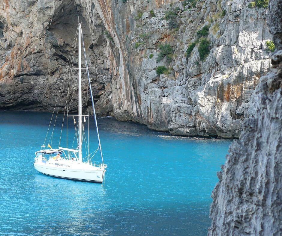 Ein weißes Segelboot auf blauem Wasser umgeben von Felsen.