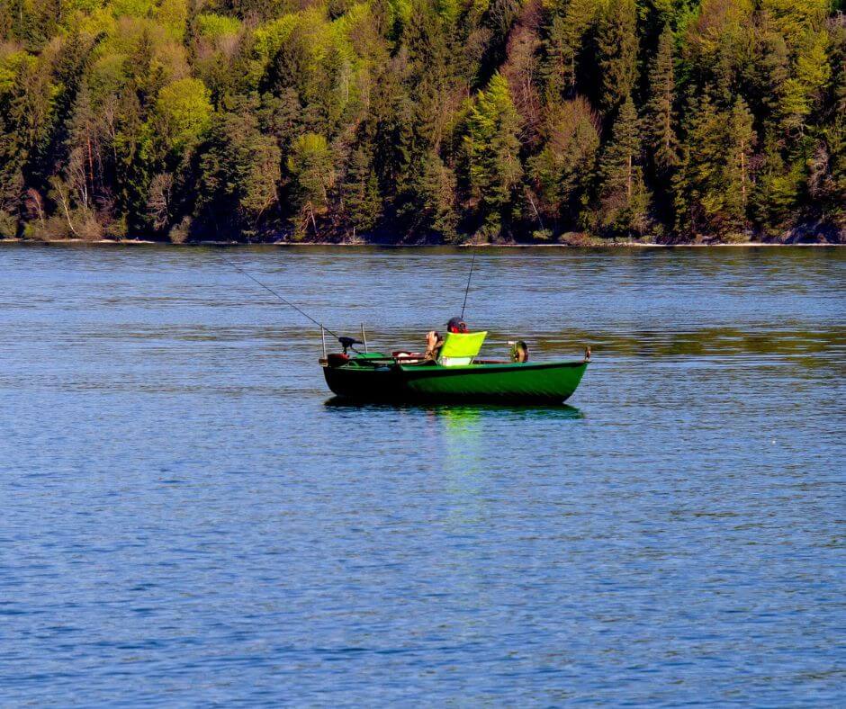 Angeln im Frühjahr vom Boot aus. Ein Boot in einem See. Im Hintergrund sieht man Bäume.