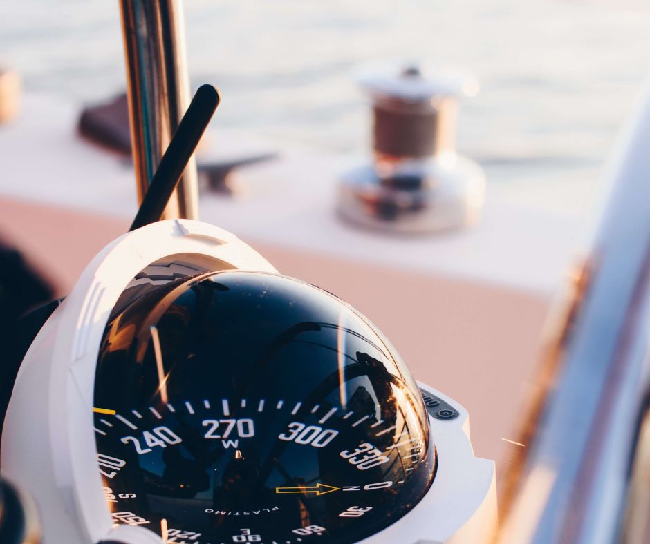 Großaufnahme eines analogen Kompasses an Board eines Bootes. Der Hintergrund ist verschwommen, jedoch befindet sich das Boot sichtlich auf dem Wasser.
