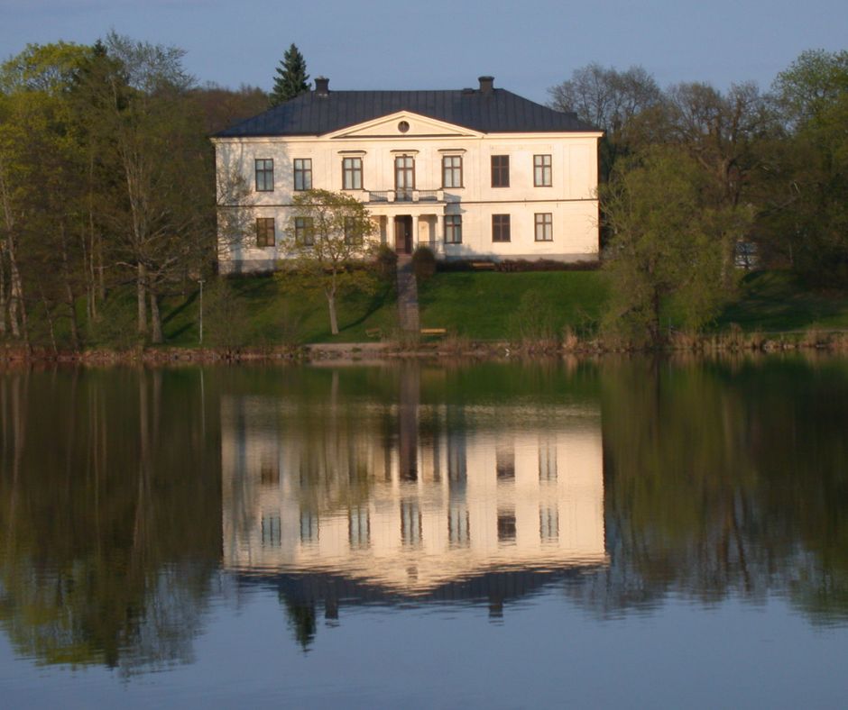 Charlottenborg Castle auf einem grünen Hügel. Davor sieht man den Götakanal, in dem sich das Schloss spiegelt.