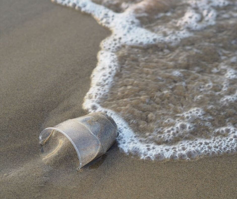 Plastikbecher am Strand, der von einer Welle umspült wird.