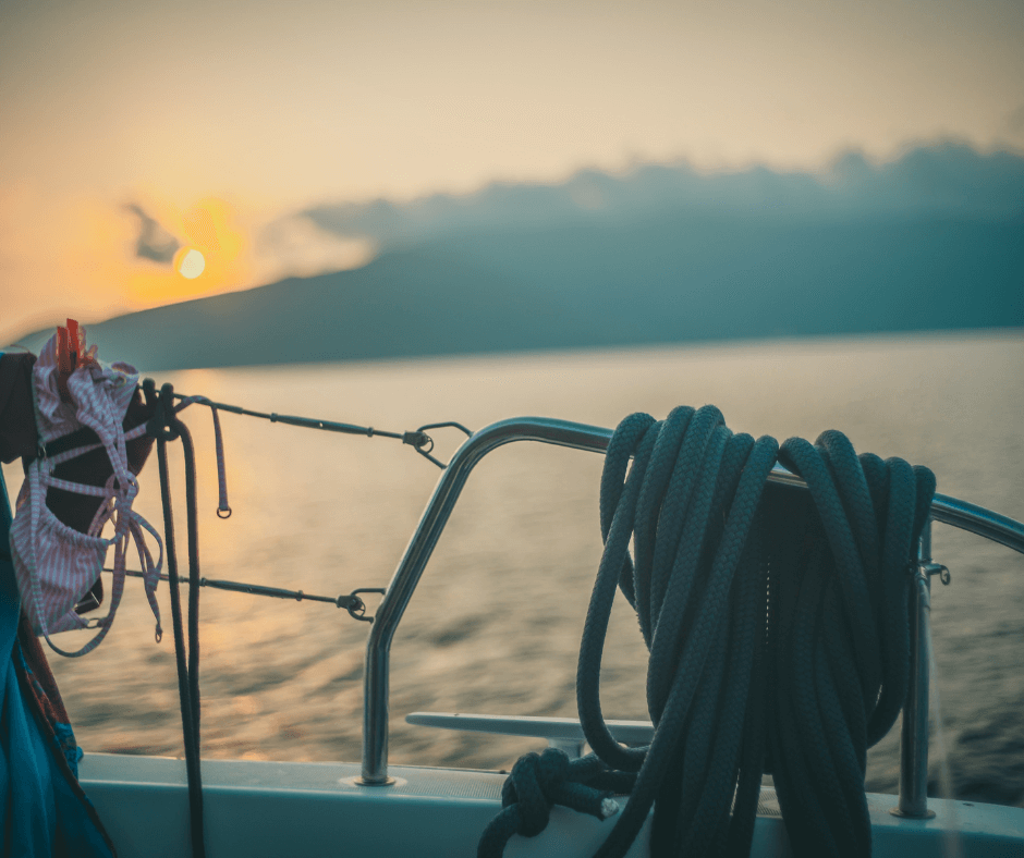 Ein Segelboot ist zu sehen und ein Sonnenuntergang im Hintergrund. Segler trocknen ihre Badekleidung während ihres Lefkada-Urlaubs. 