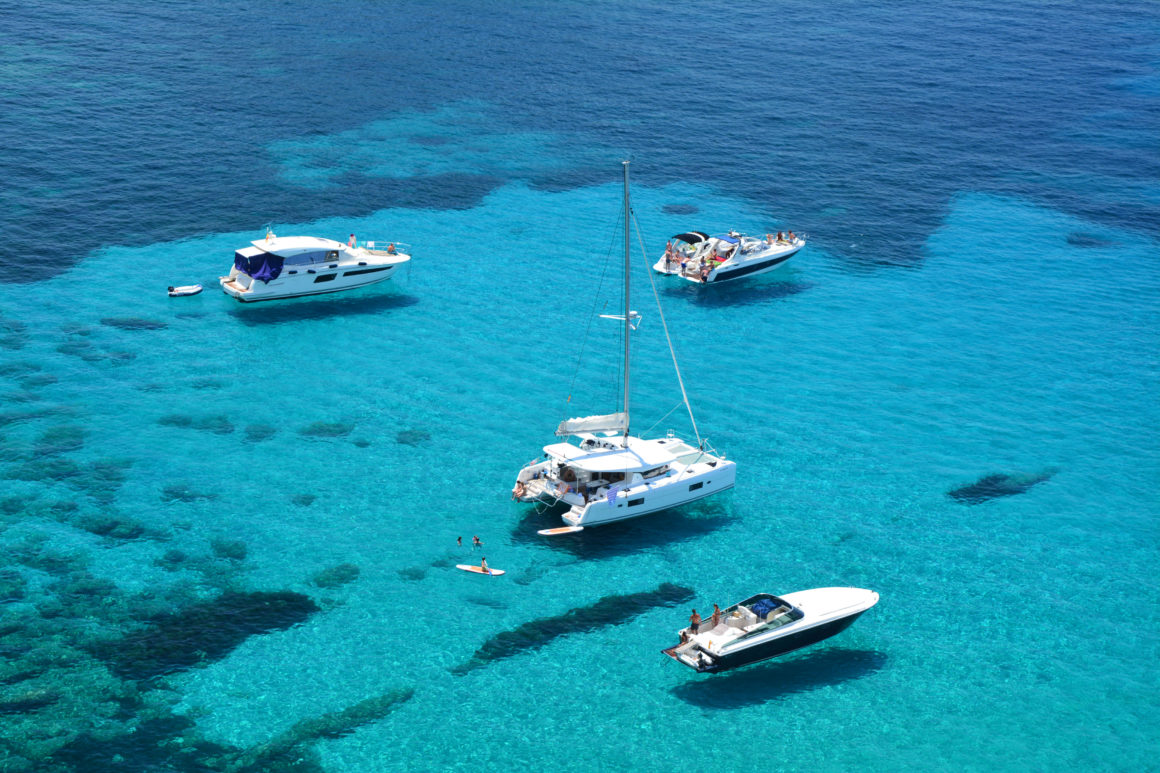 4 barcos navegando por las aguas turquesas de cala d'Hort, Ibiza. 