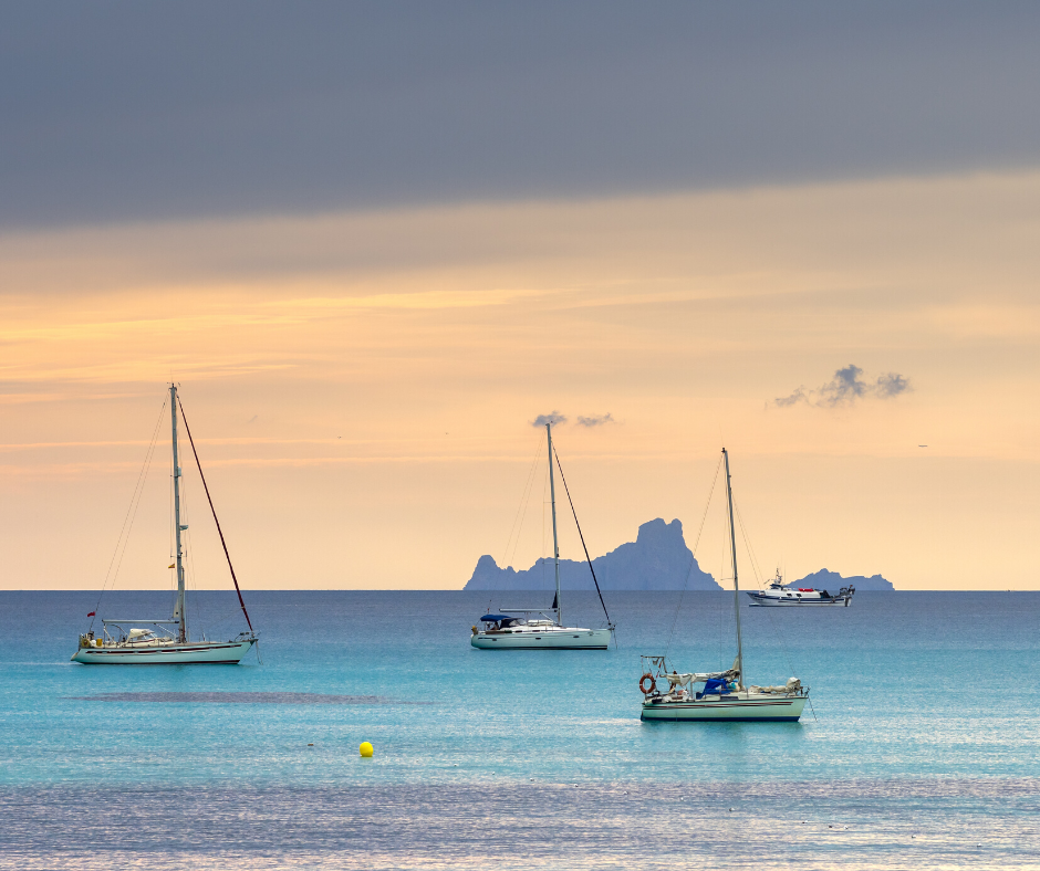 Tres veleros en Cala Saona. El cielo violeta y naranja se mezcla con el turquesa del mar. 