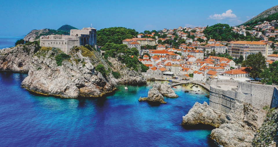  Vista desde el mar, de azul profundo, a la ciudad de Dubrovnik, con las murallas de roca gris en primer plano. 