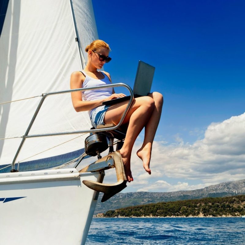 Mujer, con un ordenador, en la cubierta de un velero.