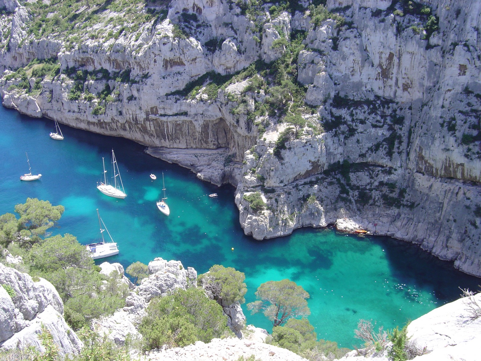 Calanque d'En Vau (Côte d'Azur) vue depuis ses hauteurs, avec des voiliers, des bateaux de plaisances et des fonds bleus