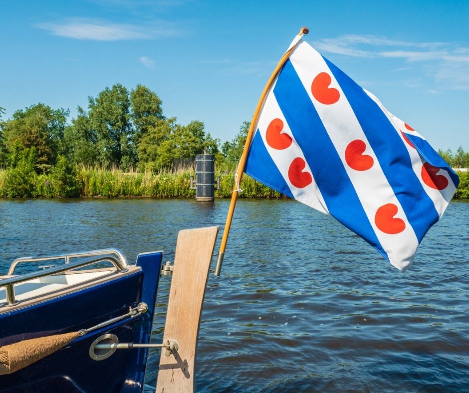 Boot met vlag van Friesland, achter landschap van groene vlakte