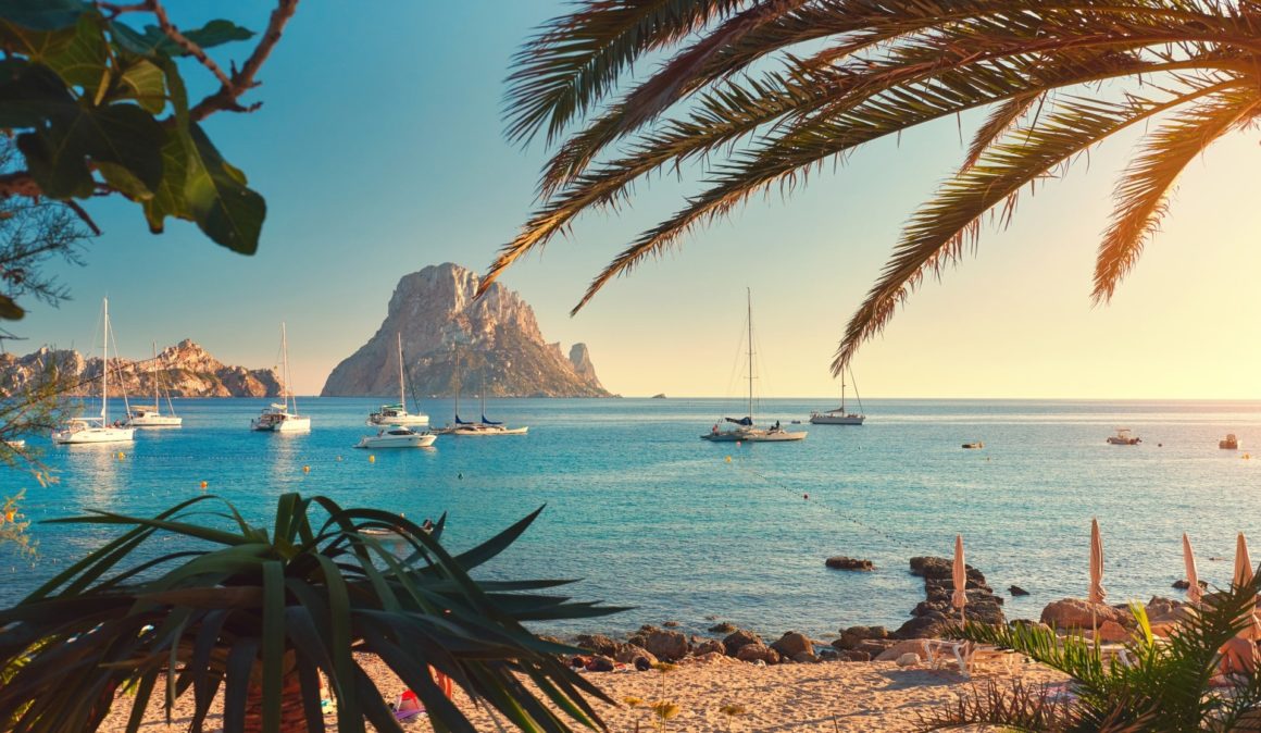 Zeilboten en motorboten in een baai op Ibiza met uitzicht op een rots.