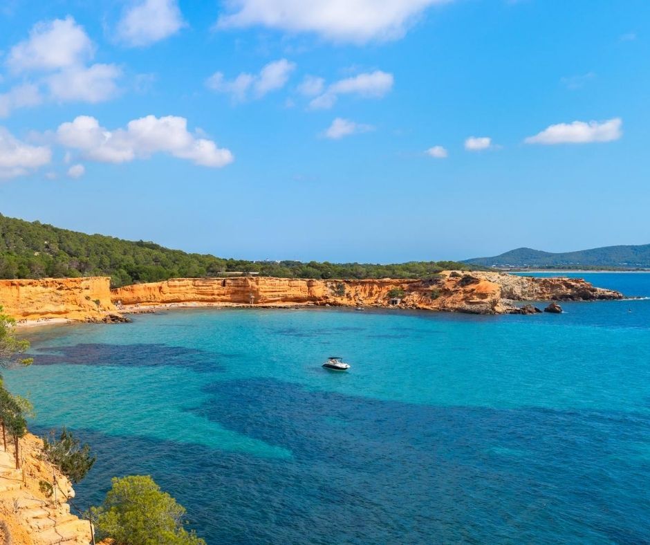 Es Bol Nou is surrounded by small cliffs formed by orange-colored clay rocks.