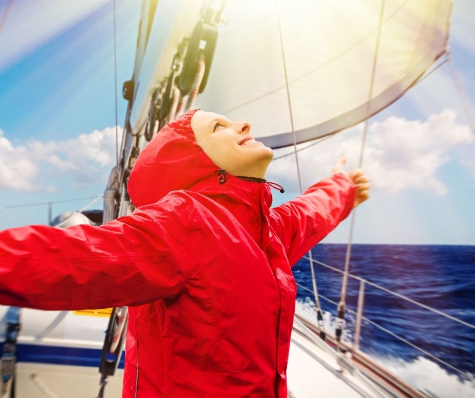 a girl on a boat in a waterproof jacket sailing and smiling