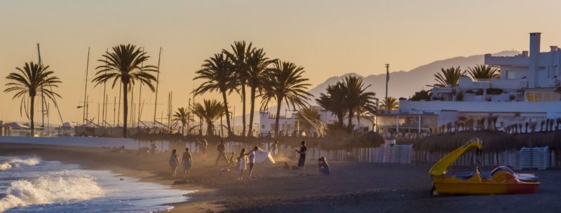 people playing on the beach of Marbella with the palms and sunset on the background