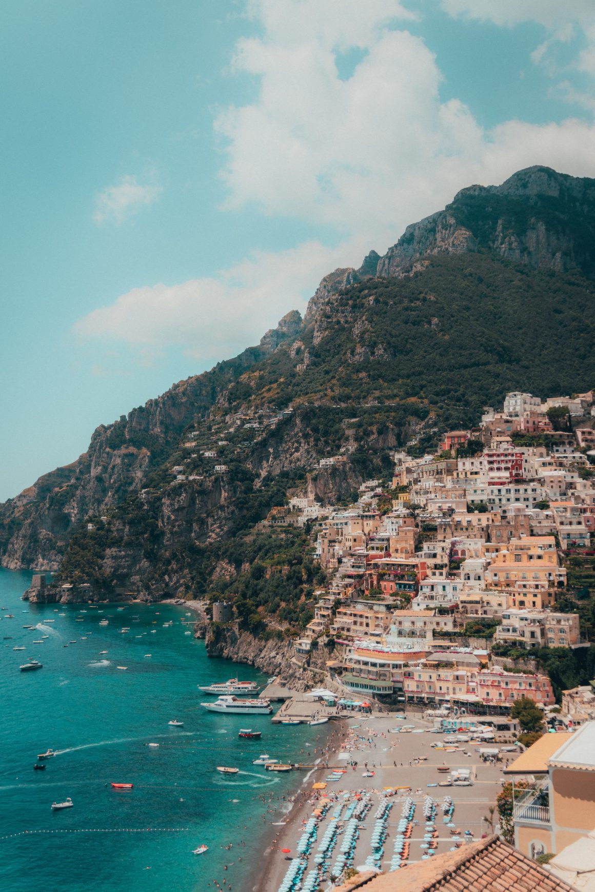 Yachts off of a beach with a backdrop of the hillside houses of Positano, Italy