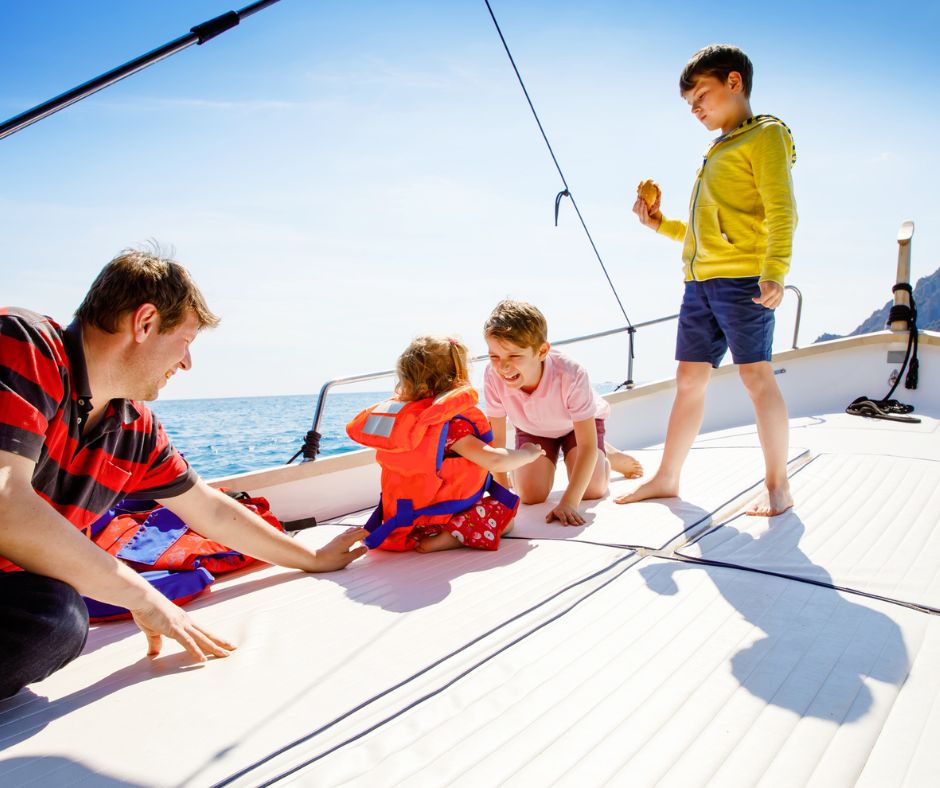 Man and three children sitting on the deck of a boat with life jackets on, sailing with your child