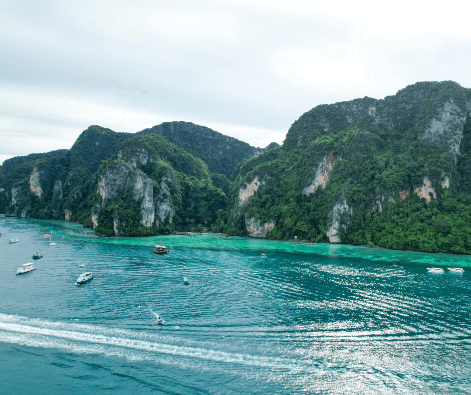 Boats at anchor in the turqoise seas of Phi Phi Island, beneath verdant cliffs. 