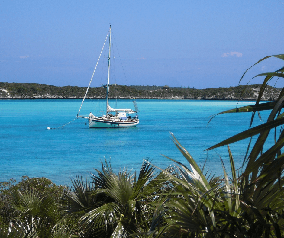 Sailboat at anchor in a bay of turquoise water, along a coast covered in palm trees. 